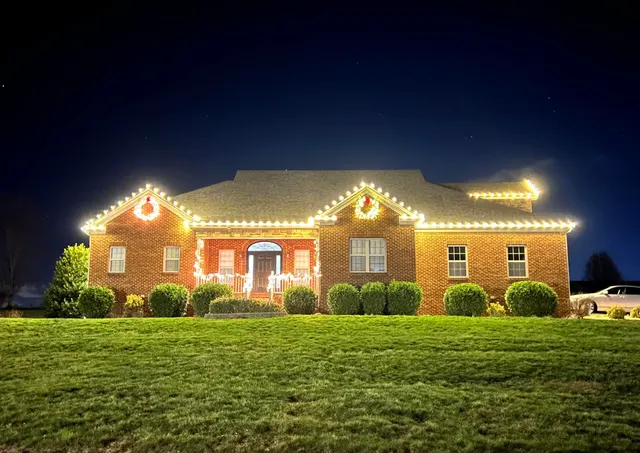 Roofline lights and illuminated wreaths above a brick home entry