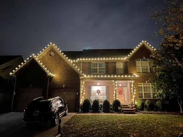 Warm white roofline lights above a two-story home and driveway
