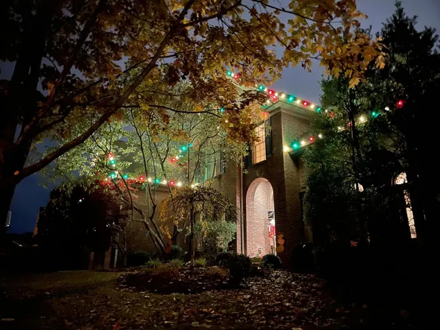 Colorful Christmas roofline lights seen through front-yard trees
