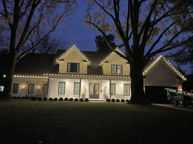 Warm white Christmas lights outlining a home and front porch at dusk