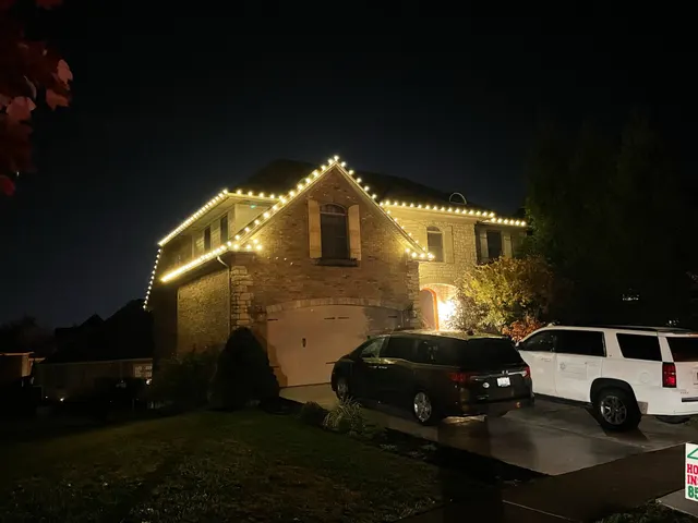 Warm holiday lights around the roof of a brick home