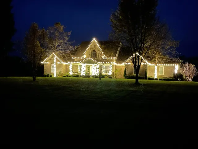 Warm roofline lights and lit trees viewed across a lawn