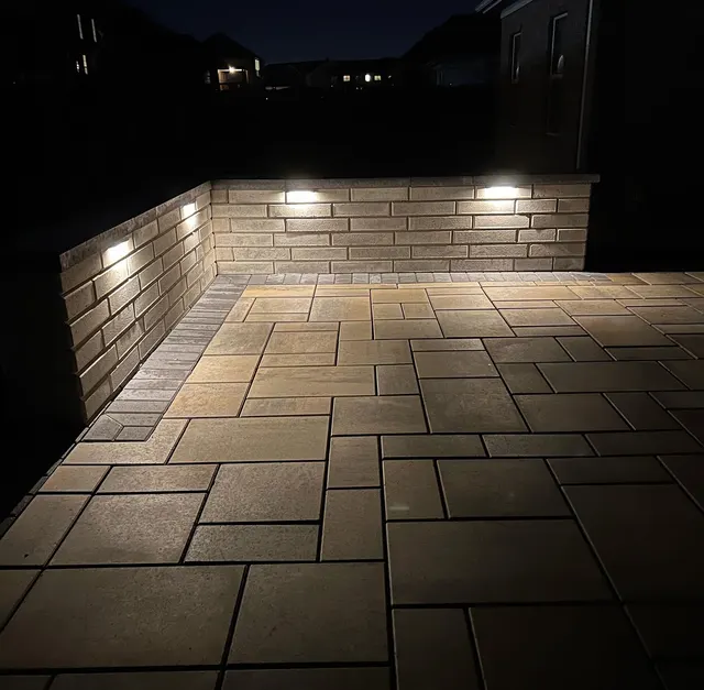 Warm wall lights above a rectangular paver patio at night