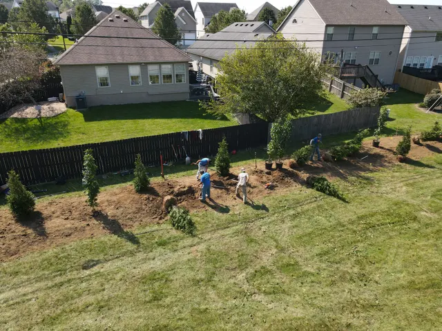 Crew preparing a landscape bed beside a backyard fence